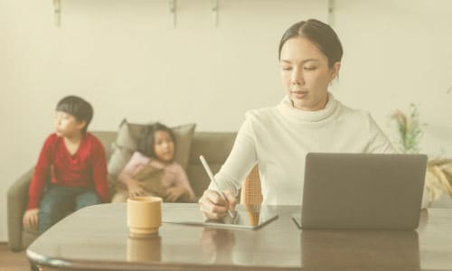 Mom at desk writing down mom blog post ideas with kids in the background